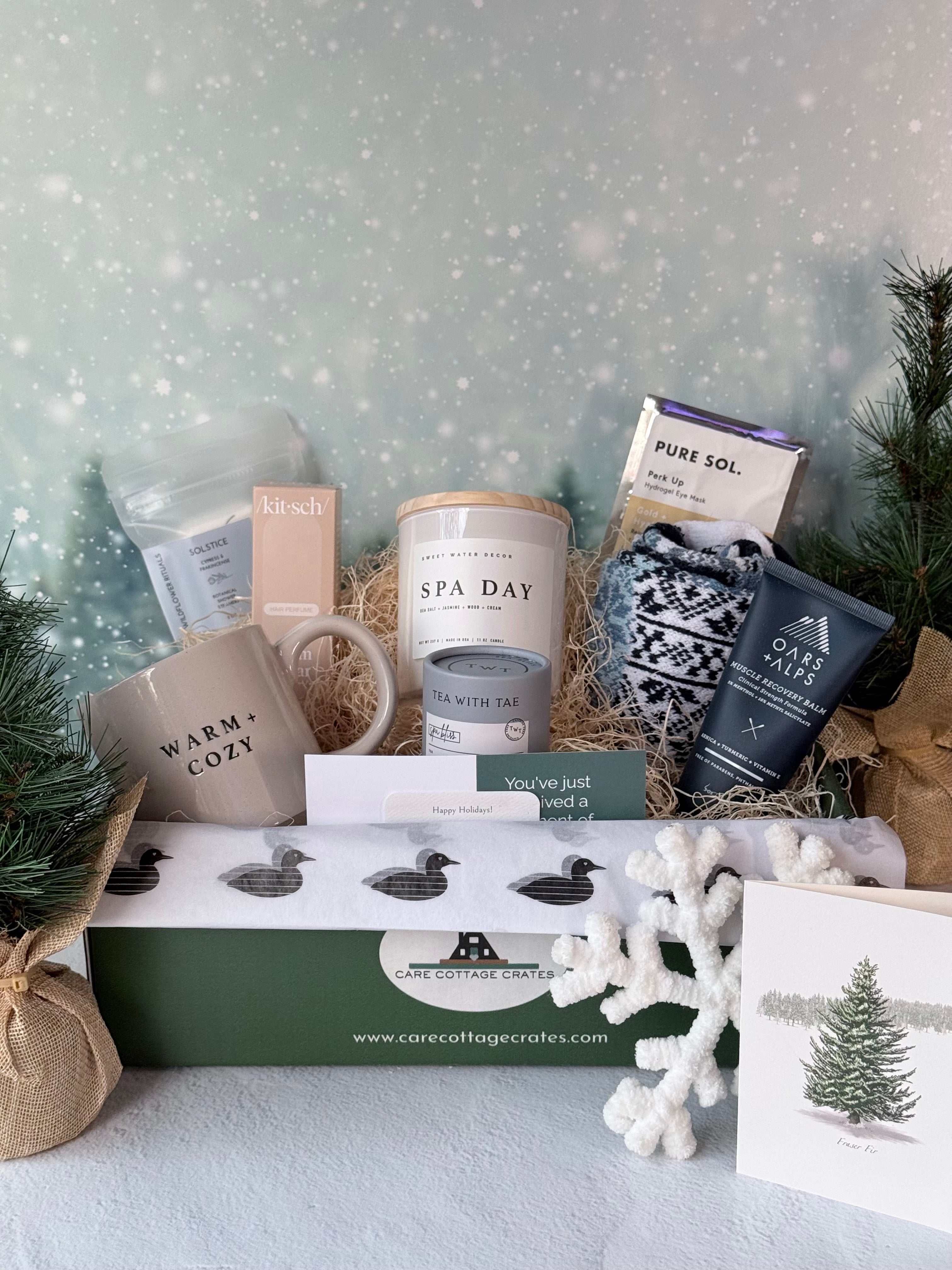 A calming spa inspired winter gift crate displayed in a green Care Cottage Crates box with pine branches. Includes Solstice shower steamers, Kitsch Warm Sugar hair perfume, a Sweet Water Decor Spa Day candle, Tea with Tae Spa Bliss tea tube, a Pure Sol eye mask, Solmate Snowdrop socks and an Oars and Alps muscle recovery balm.