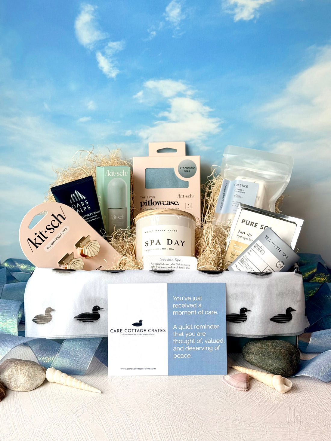 Crate full of self care goodies including Kitsch Seashell Hair Clips, Oars and Alps Muscle Recovery Balm, Kitsch Hair Perfume, Kitsch Pillowcase, Sweet Water Decor Candle, Wildflower Rituals Shower Steamers, Pure Sol Eye Mask, and Tea with Tae Spa Bliss Tea Tube.